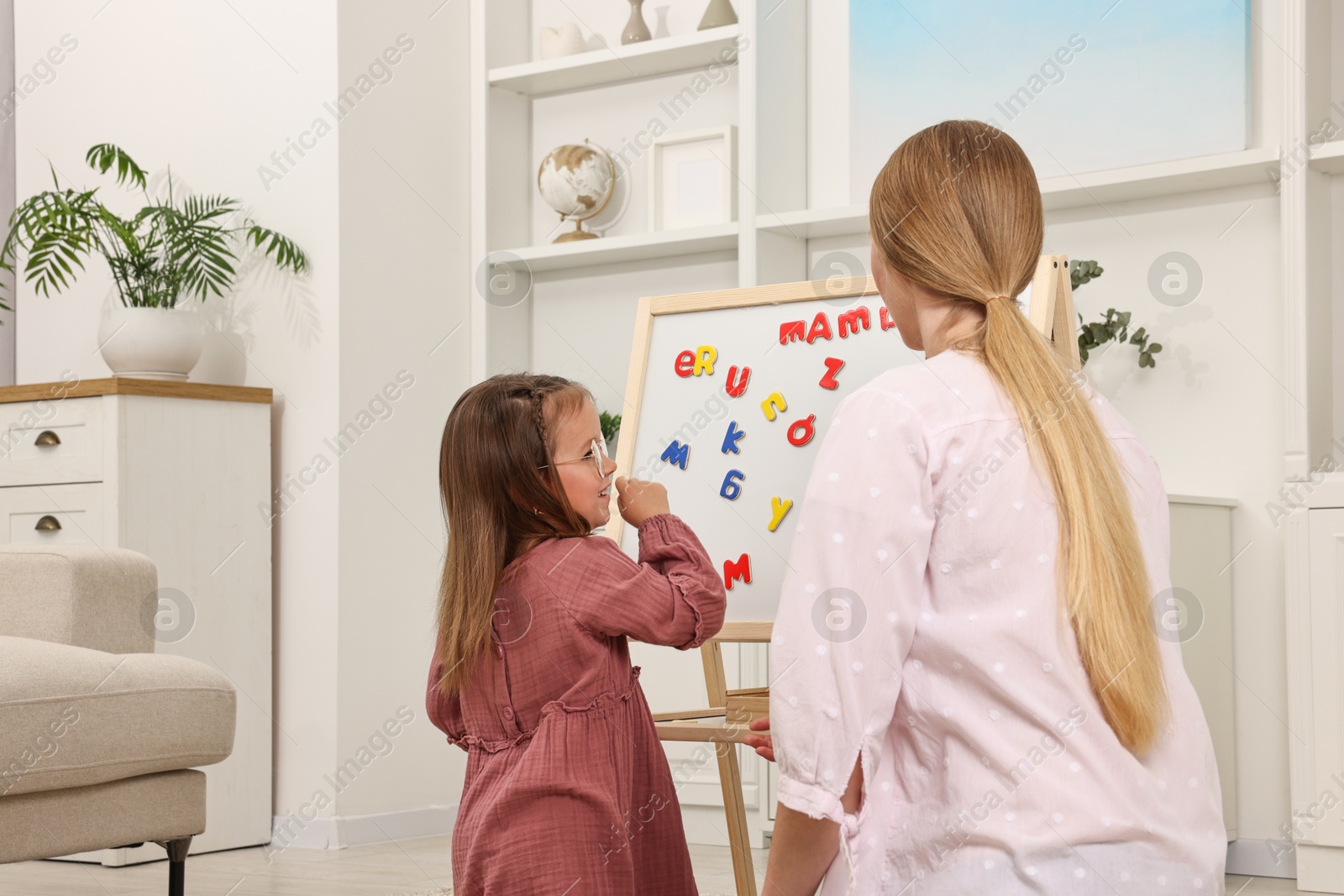 Photo of Mom teaching her daughter alphabet with magnetic letters at home