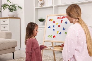 Photo of Mom teaching her daughter alphabet with magnetic letters at home