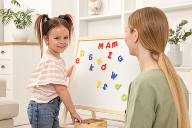 Photo of Mom teaching her daughter alphabet with magnetic letters at home