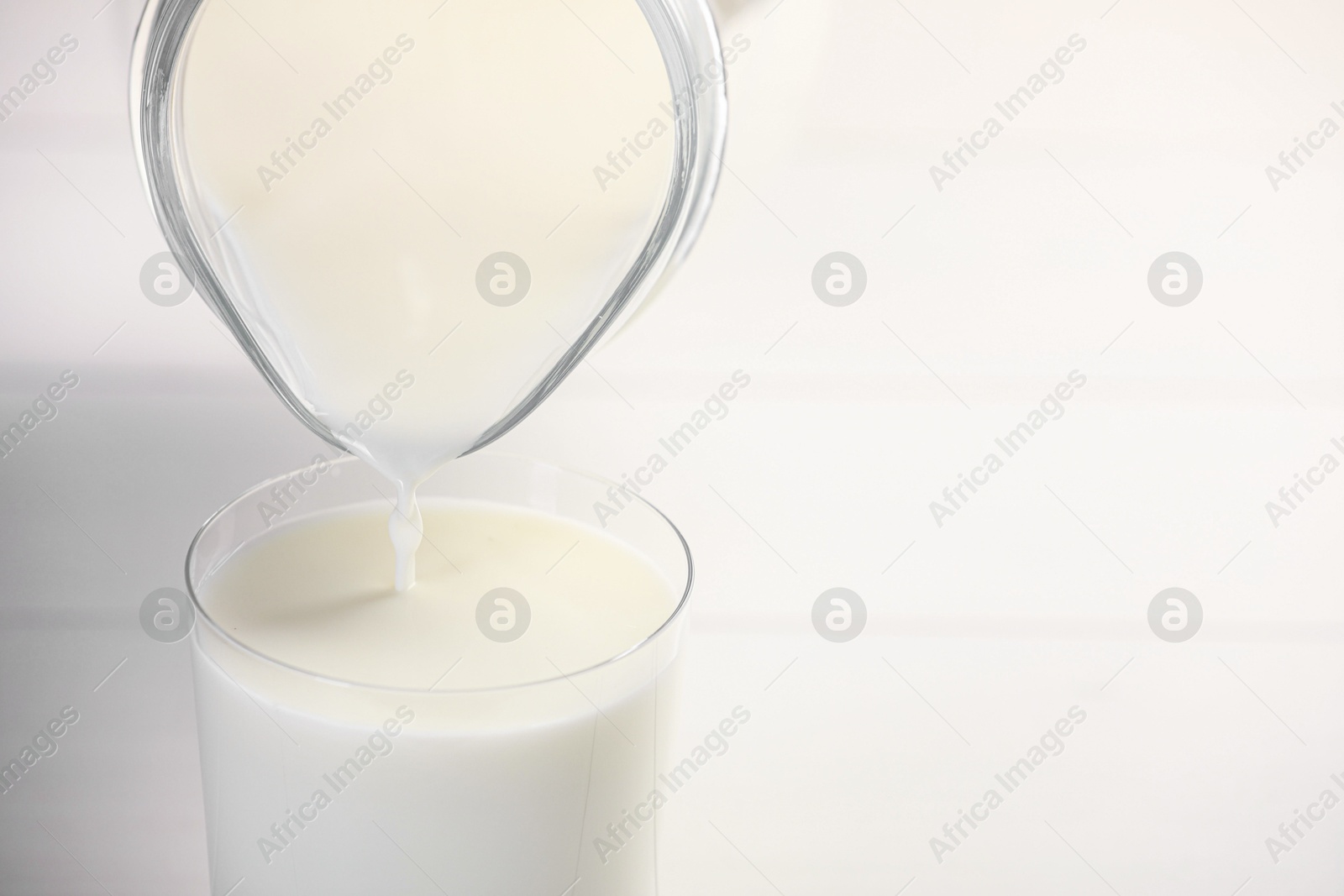 Photo of Pouring fresh milk from jug into glass at white table, closeup. Space for text