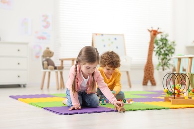 Cute little children playing together on puzzle mat in kindergarten