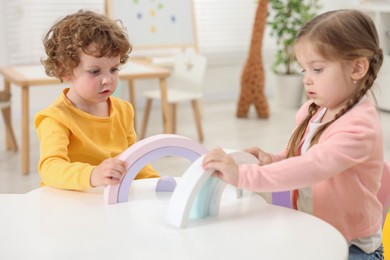 Photo of Cute little children playing with colorful toy rainbow at white table in kindergarten