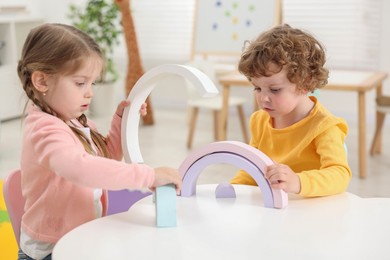 Photo of Cute little children playing with colorful toy rainbow at white table in kindergarten