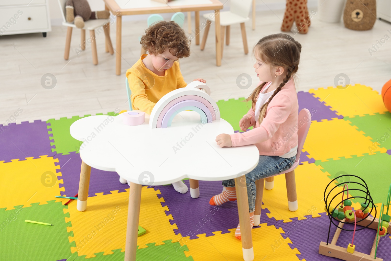 Photo of Cute little children playing with colorful toy rainbow at white table in kindergarten