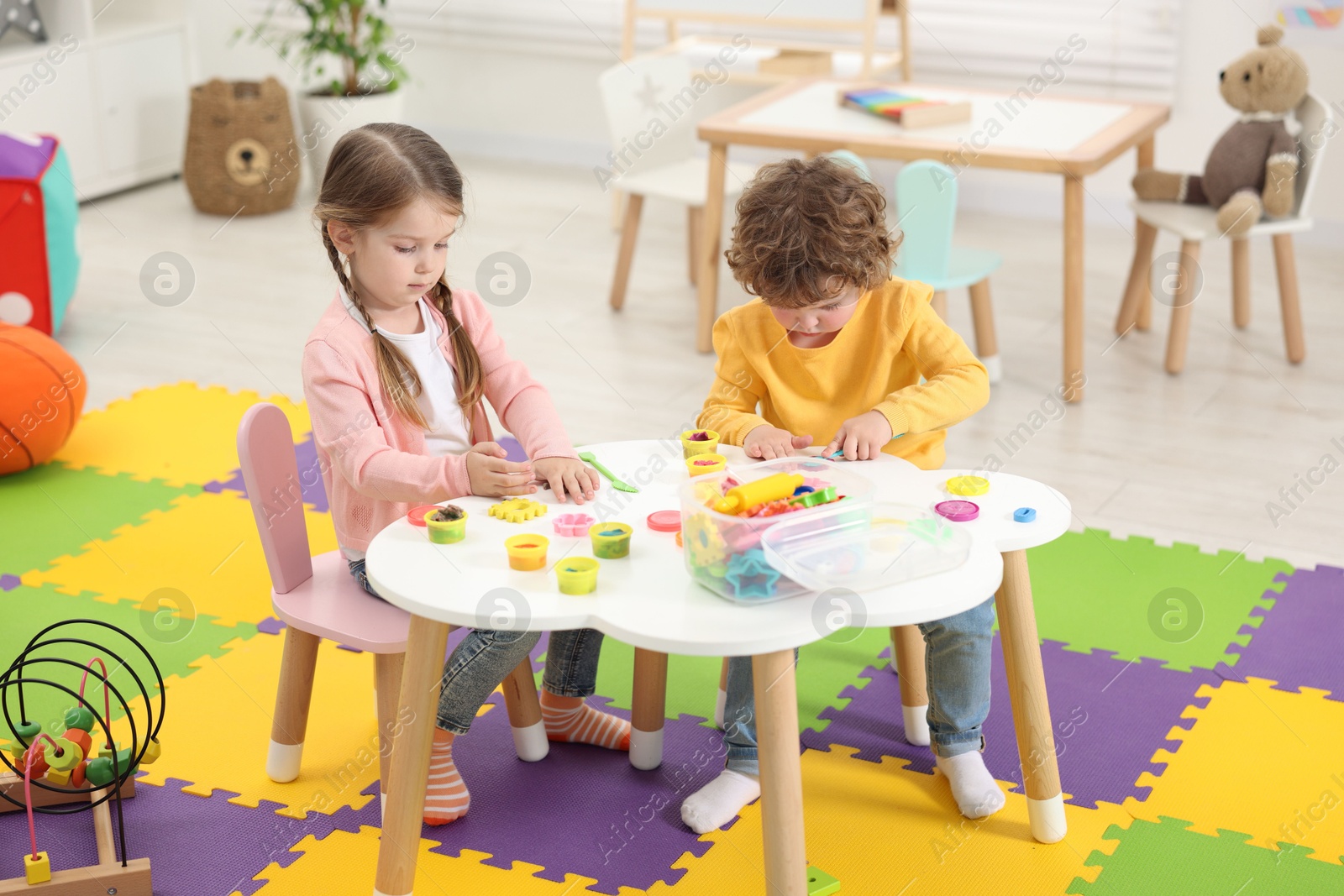 Photo of Cute little children modeling from plasticine at white table in kindergarten