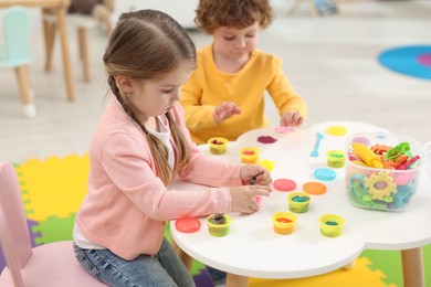 Photo of Cute little children modeling from plasticine at white table in kindergarten