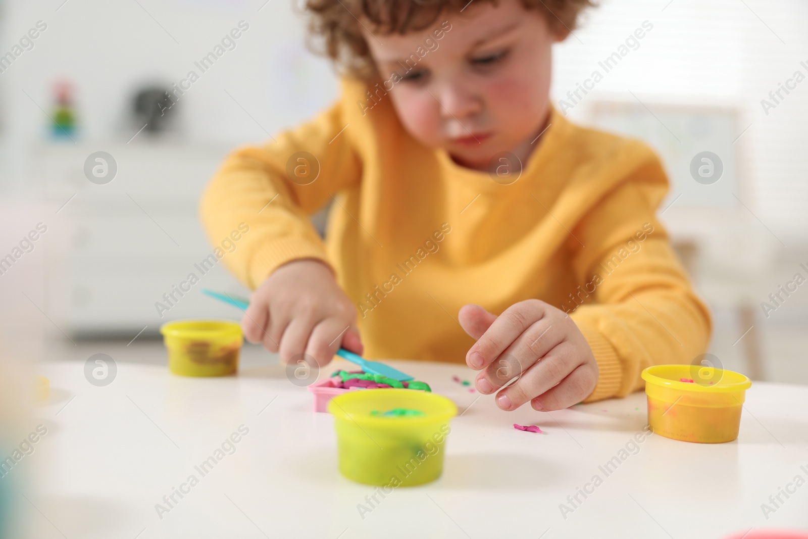 Photo of Little boy modeling from plasticine at white table in kindergarten, closeup