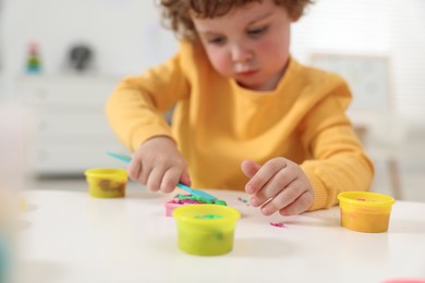 Photo of Little boy modeling from plasticine at white table in kindergarten, closeup