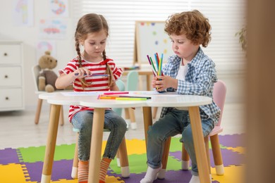 Photo of Cute little children drawing with colorful pencils at white table in kindergarten