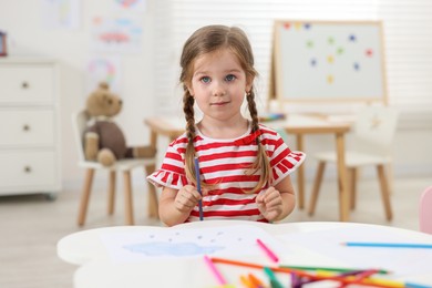 Photo of Cute little girl drawing at white table in kindergarten