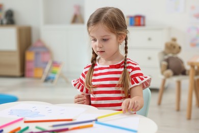 Cute little girl drawing at white table in kindergarten