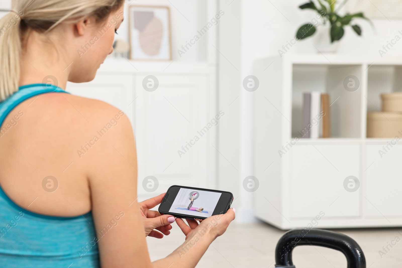 Photo of Online fitness trainer. Woman watching tutorial on smartphone at home