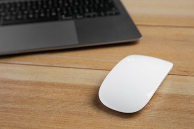 Photo of Wireless mouse and laptop on wooden table, closeup