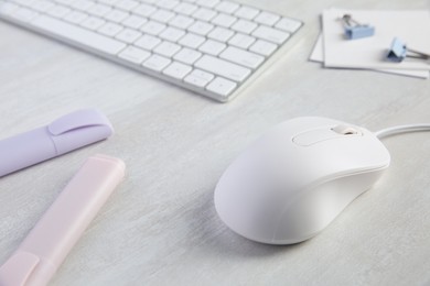 Photo of Wired mouse, stationery and computer keyboard on light wooden table, closeup