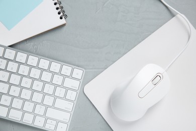 Photo of Wired mouse with mousepad, notebook and computer keyboard on grey textured table, flat lay