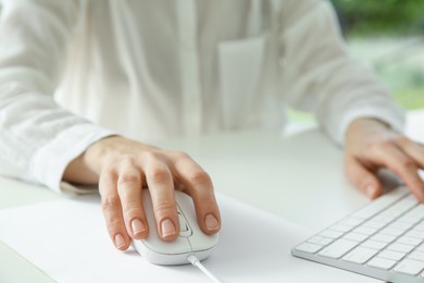 Woman working with wired mouse and computer keyboard at white table indoors, closeup