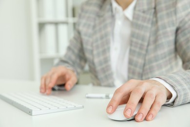 Photo of Woman working with wireless mouse and computer keyboard at white table indoors, closeup