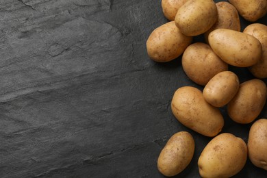 Photo of Many fresh potatoes on black textured table, top view. Space for text