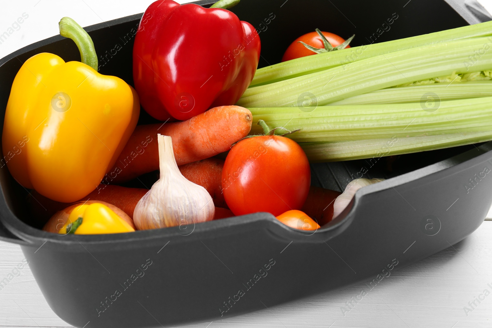 Photo of Black pot with fresh vegetables on white wooden table