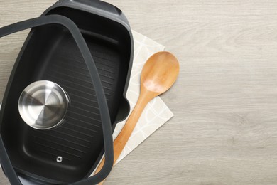 Photo of Black pot with glass lid and spoon on wooden table, top view