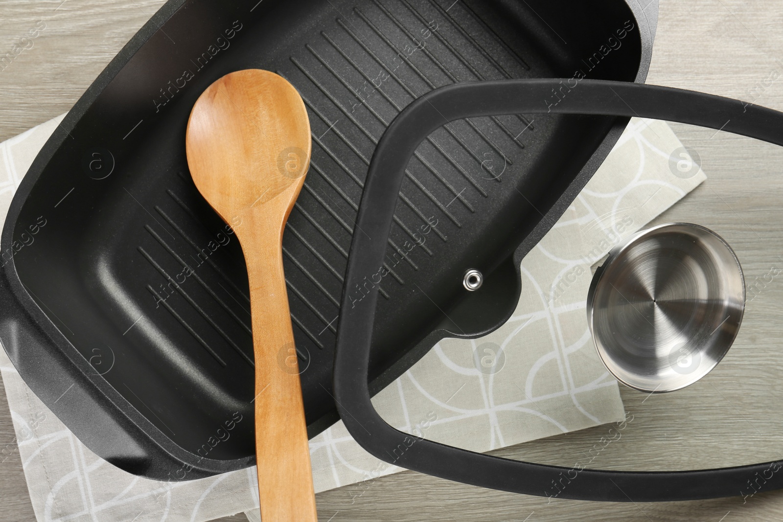 Photo of Black pot with glass lid and spoon on wooden table, top view