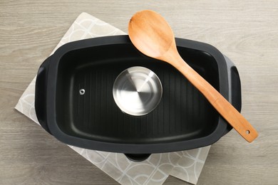 Photo of Black pot with glass lid and spoon on wooden table, top view