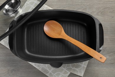 Photo of Black pot with glass lid and spoon on wooden table, top view