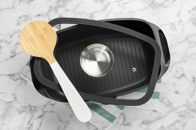 Black pot with glass lid and round spatula on white marble table, flat lay