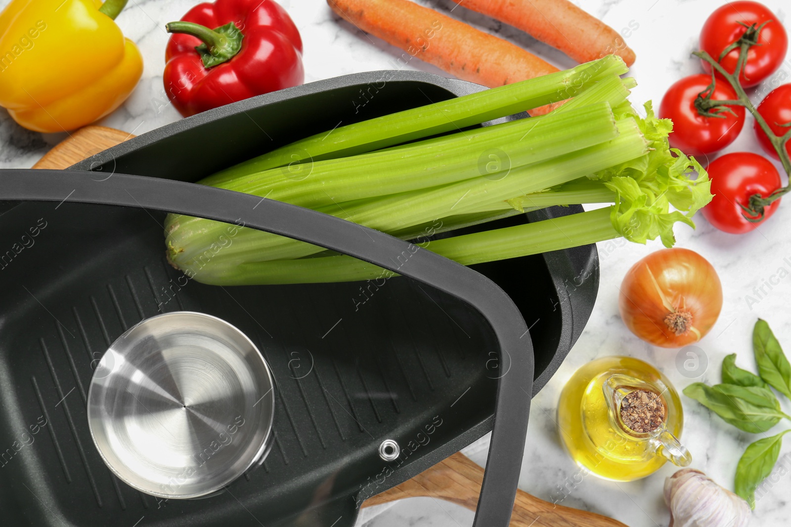 Photo of Black pot with glass lid, spices and vegetables on white marble table, flat lay