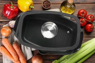 Photo of Black pot with glass lid, spices and vegetables on wooden table, flat lay