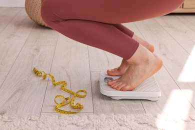 Photo of Woman on floor scale and measuring tape at home, closeup. Weight control