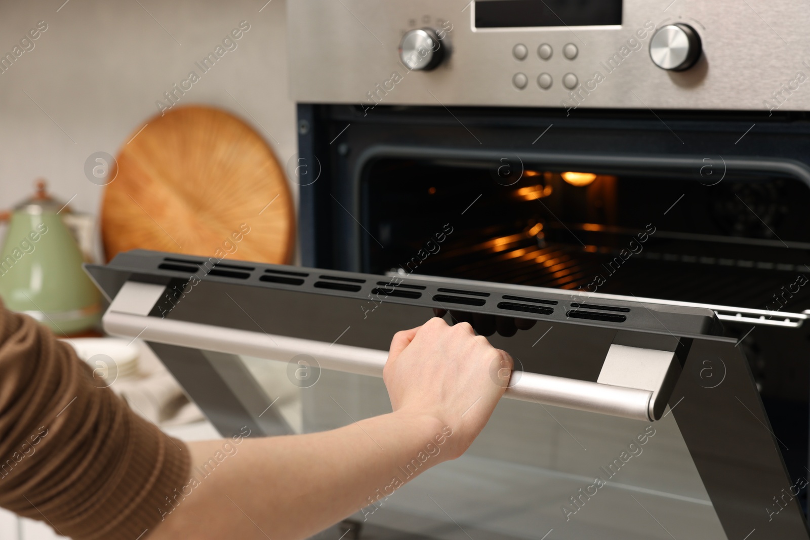 Photo of Woman using electric oven in kitchen, closeup