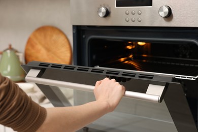 Photo of Woman using electric oven in kitchen, closeup