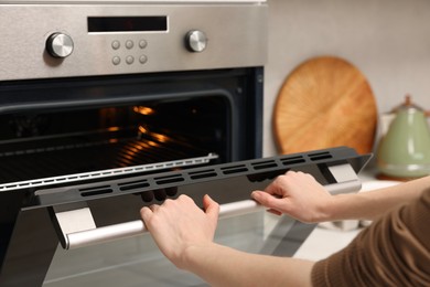 Woman using electric oven in kitchen, closeup