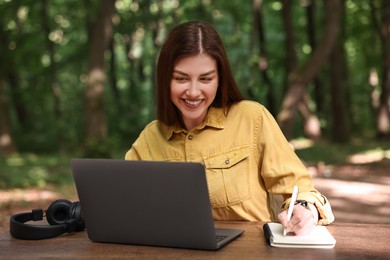 Photo of Smiling freelancer working with laptop and writing something at table outdoors. Remote job