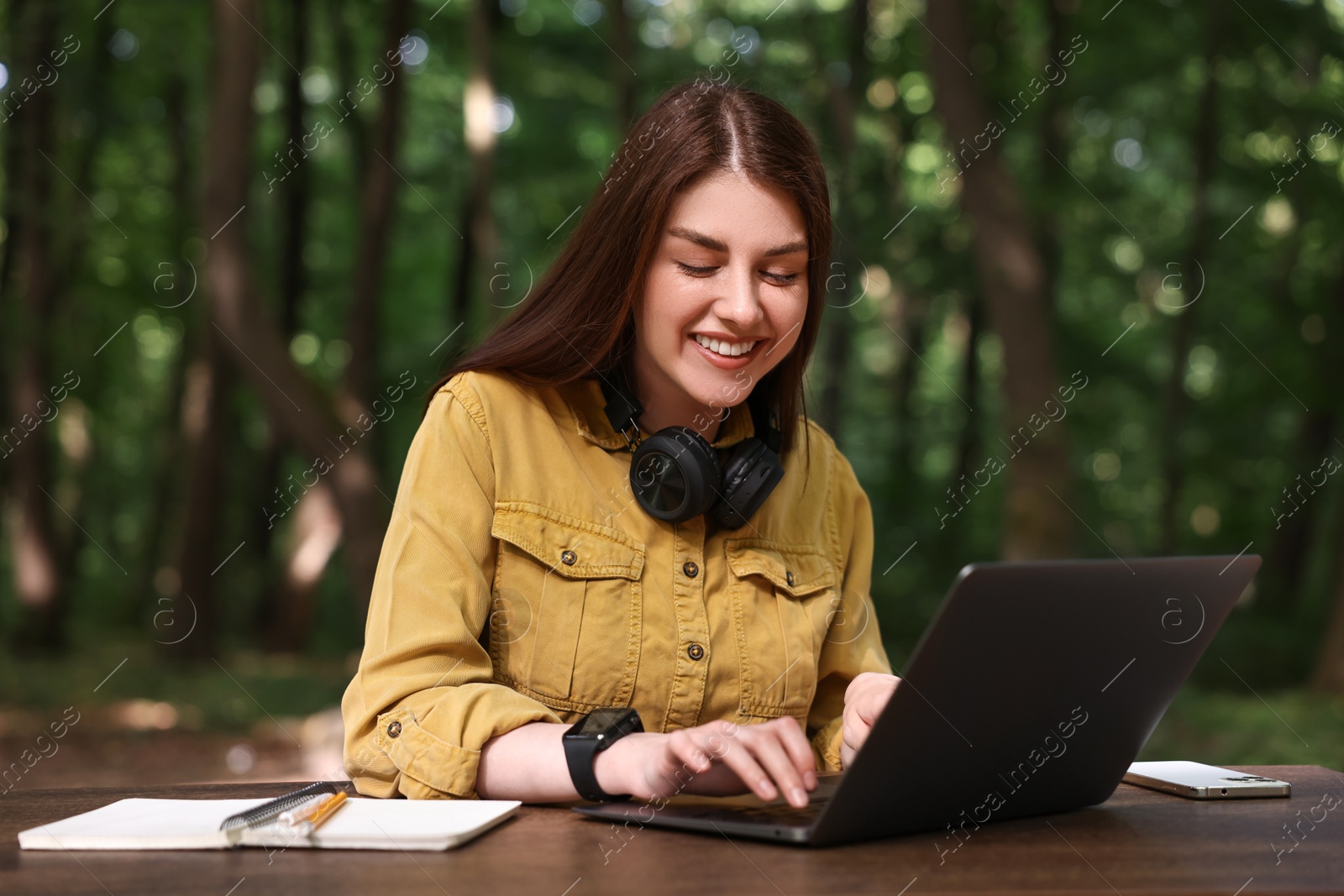 Photo of Smiling freelancer working with laptop at table outdoors. Remote job