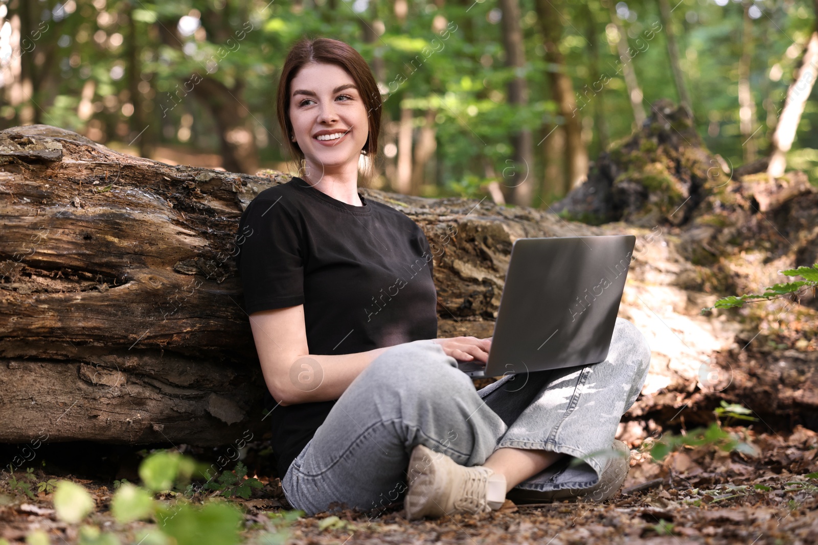 Photo of Smiling freelancer working with laptop in forest. Remote job