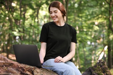 Smiling freelancer working with laptop in forest, low angle view. Remote job