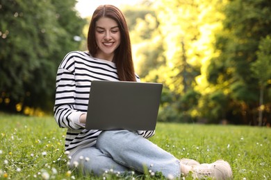 Smiling freelancer working with laptop on green grass outdoors, space for text. Remote job