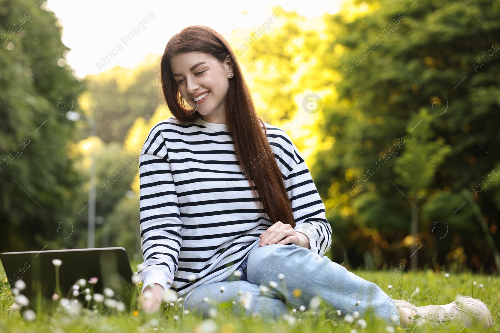Photo of Smiling freelancer working with laptop on green grass outdoors, low angle view. Remote job
