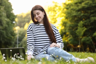 Photo of Smiling freelancer working with laptop on green grass outdoors, low angle view. Remote job