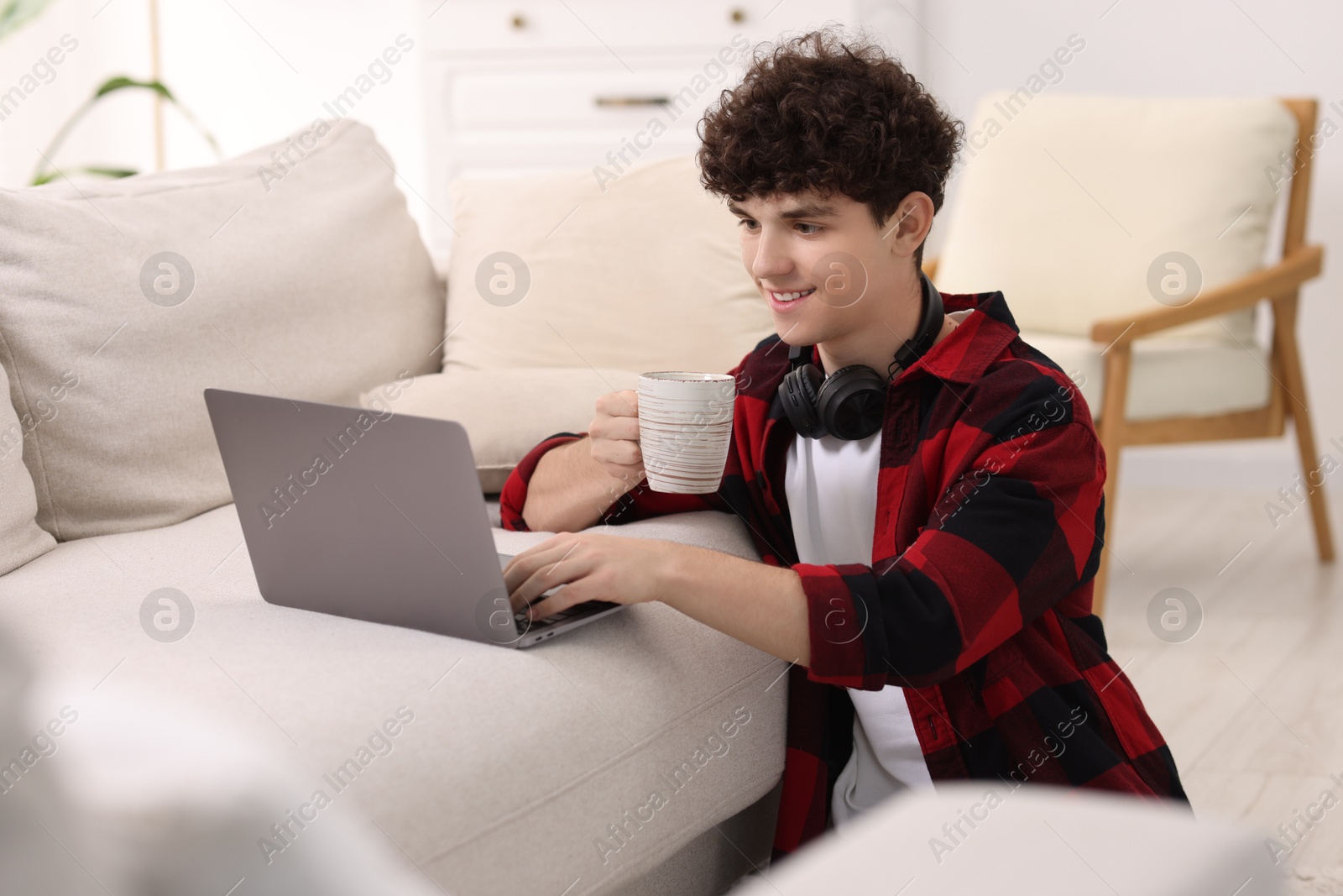 Photo of Teenager with cup of drink working on laptop at home. Remote job