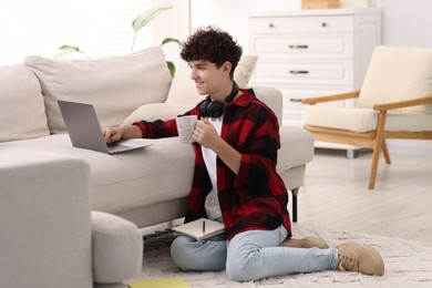 Teenager with cup of drink working on laptop at home. Remote job