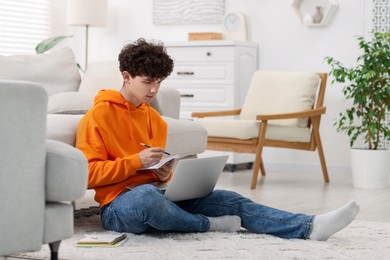 Teenager taking notes while working with laptop at home. Remote job