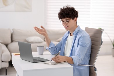 Teenager taking notes while working with laptop on sofa at home. Remote job