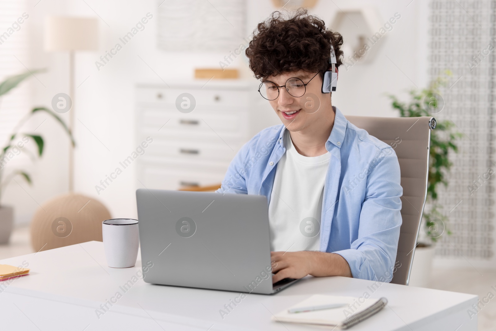 Photo of Teenager in headphones working with laptop at home. Remote job