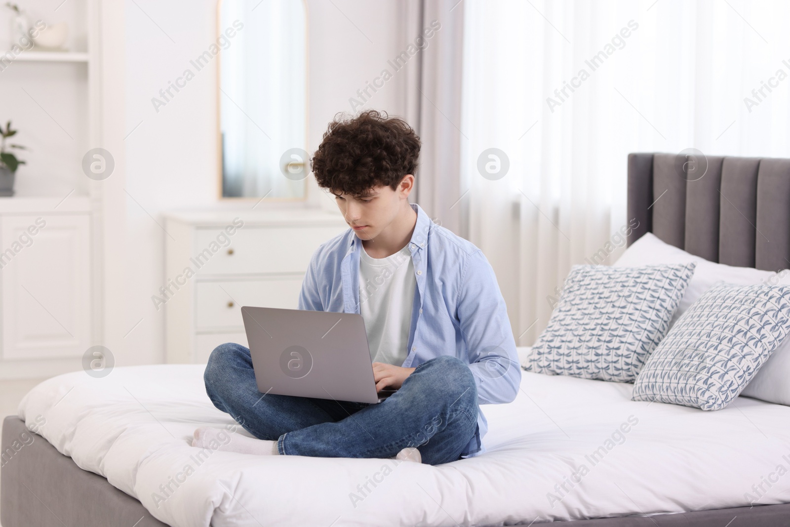 Photo of Teenager working with laptop on bed at home. Remote job