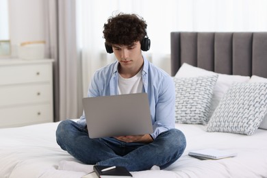 Teenager in headphones working with laptop on bed at home. Remote job