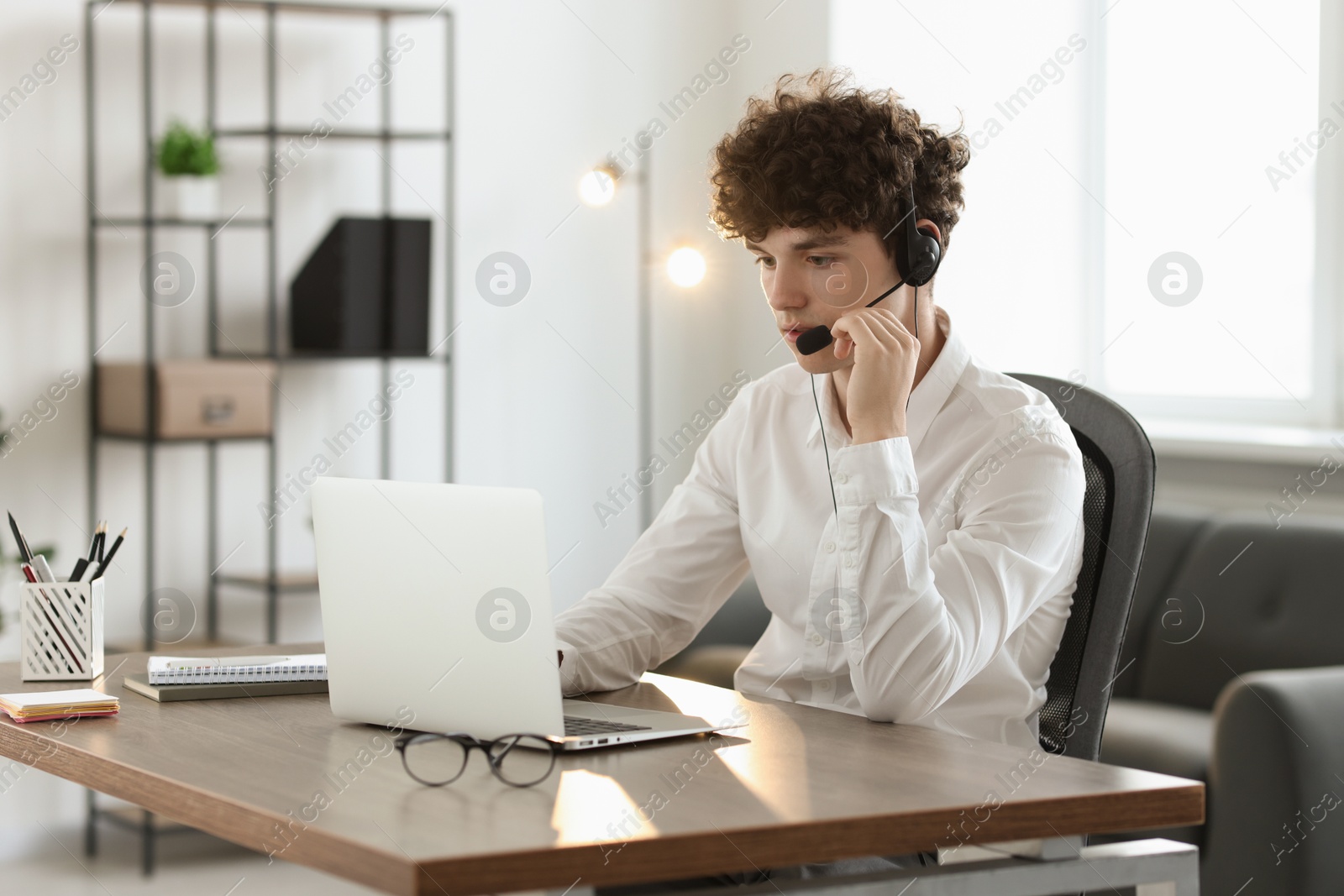 Photo of Teenager in headset working with laptop at table indoors. Remote job