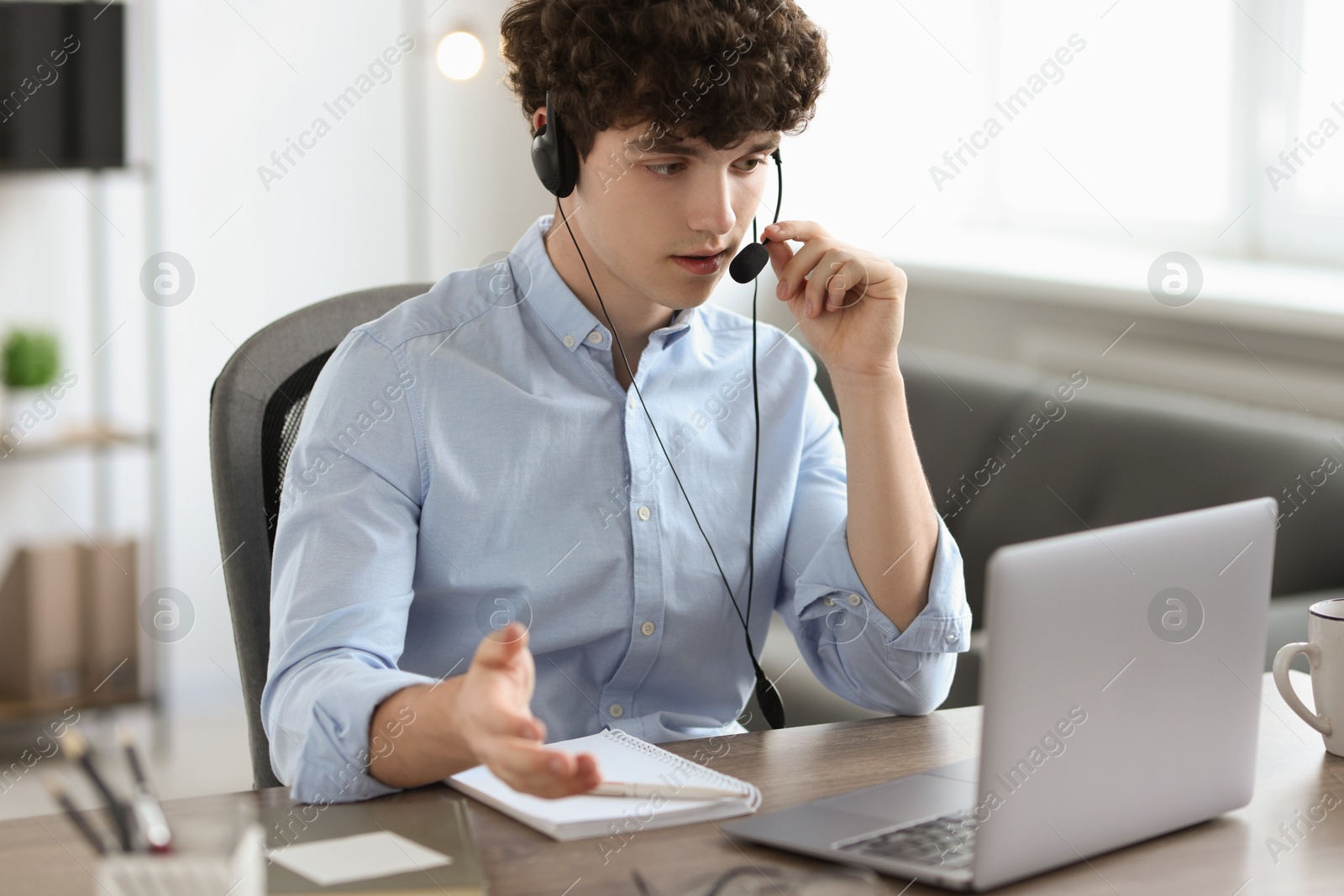 Photo of Teenager in headset having video chat via laptop at table indoors. Remote work